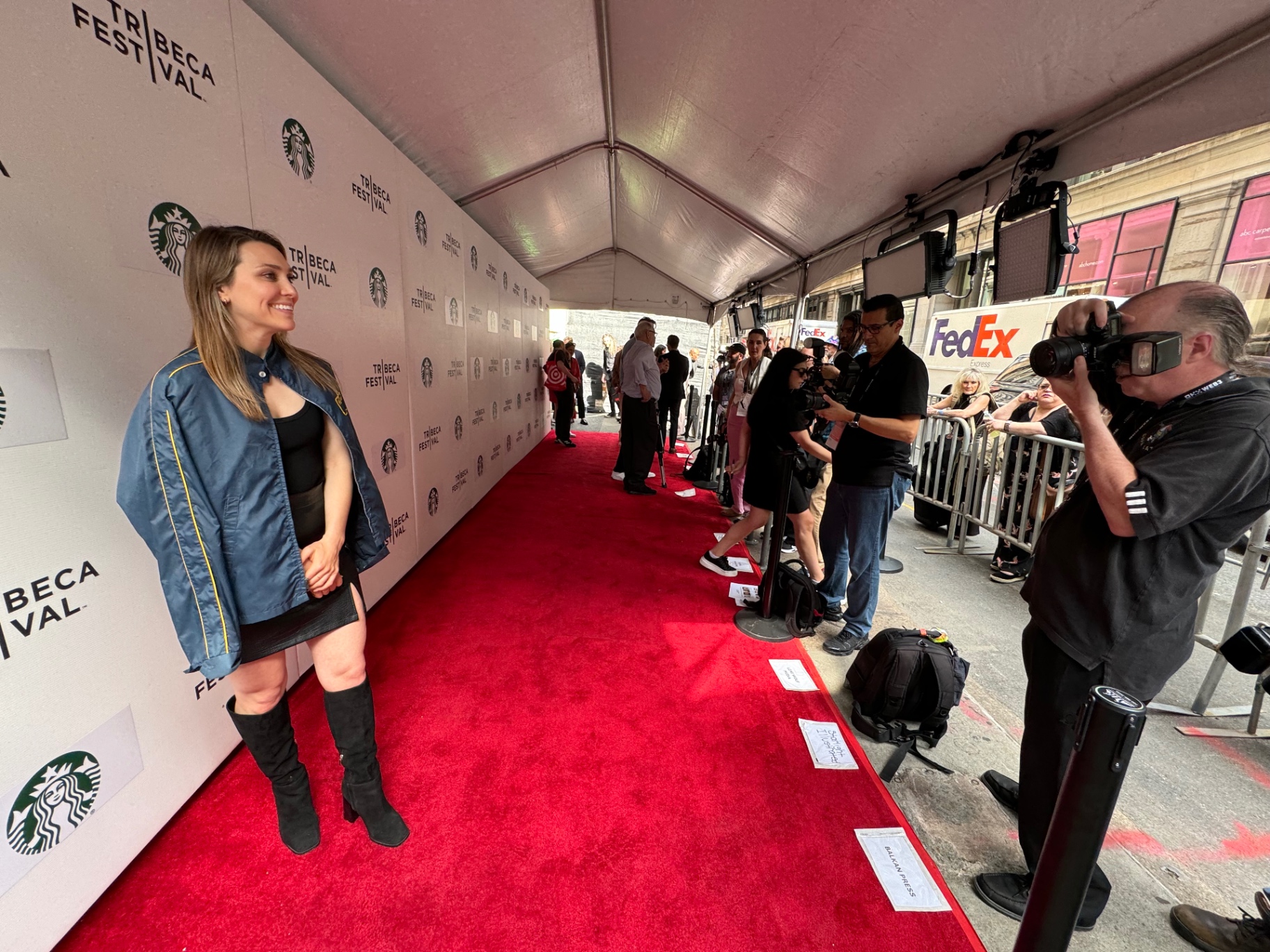 Talent poses on the Tribeca Festival red carpet step-and-repeat as a photographer captures the image.