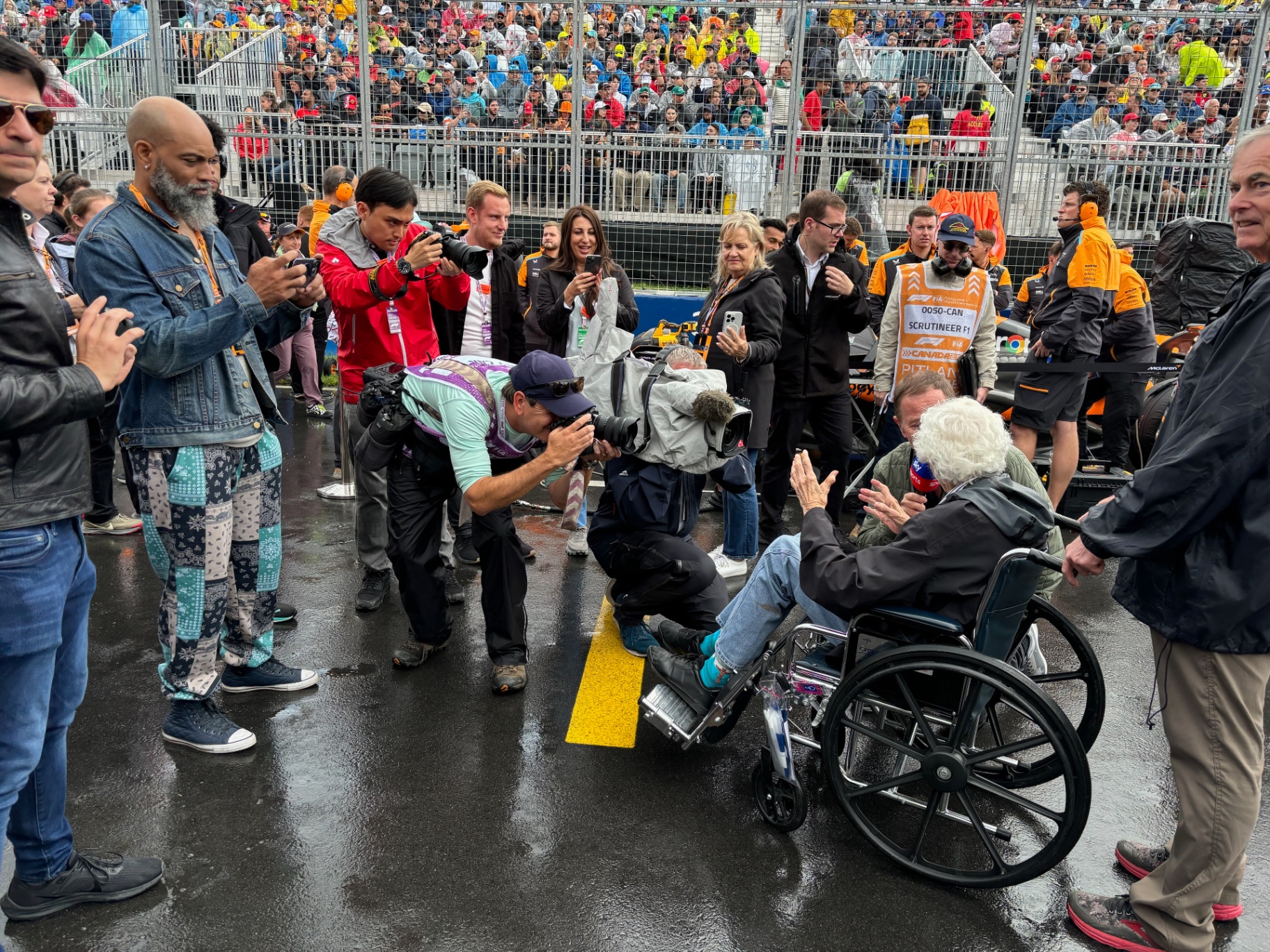 Photographers and broadcast crews crowd a wheelchair-bound legend on the F1 Canadian Grand Prix grid.