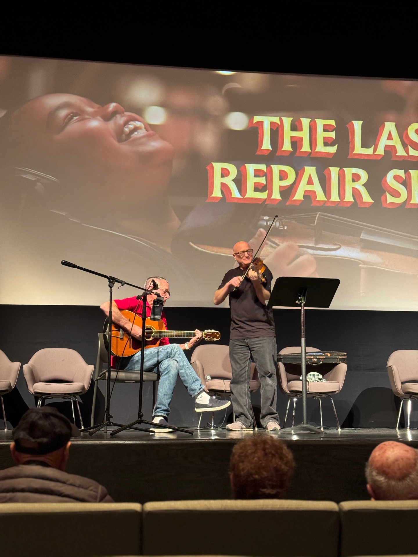 Live guitar and violin performance onstage beneath The Last Repair Shop screen during an awards-season event