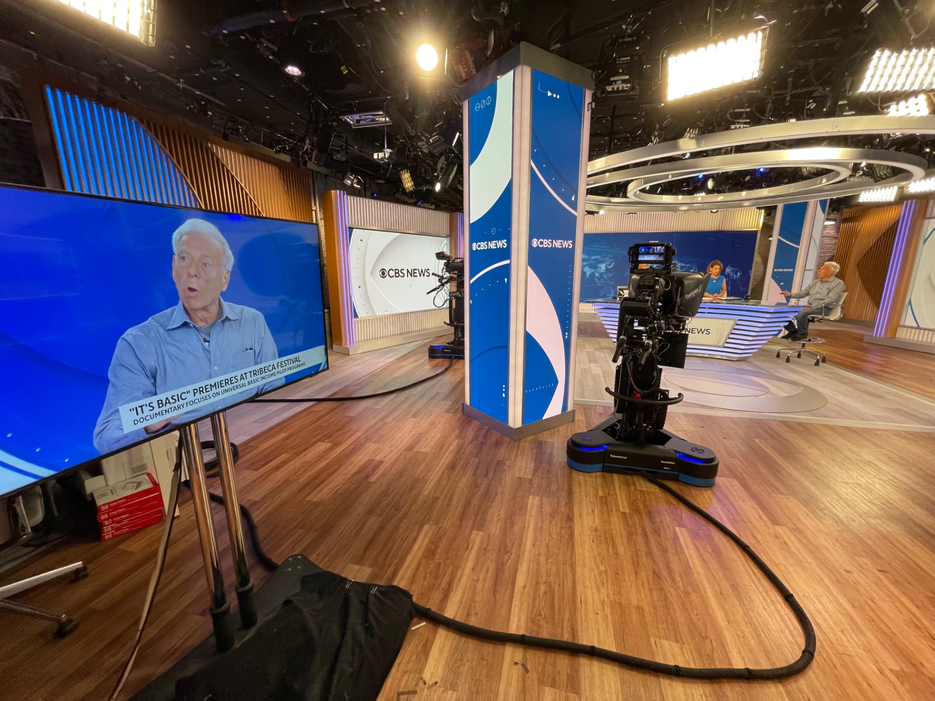 CBS News studio with It's Basic premieres at Tribeca Festival lower-third graphic on the monitor and the live interview at the anchor desk behind.