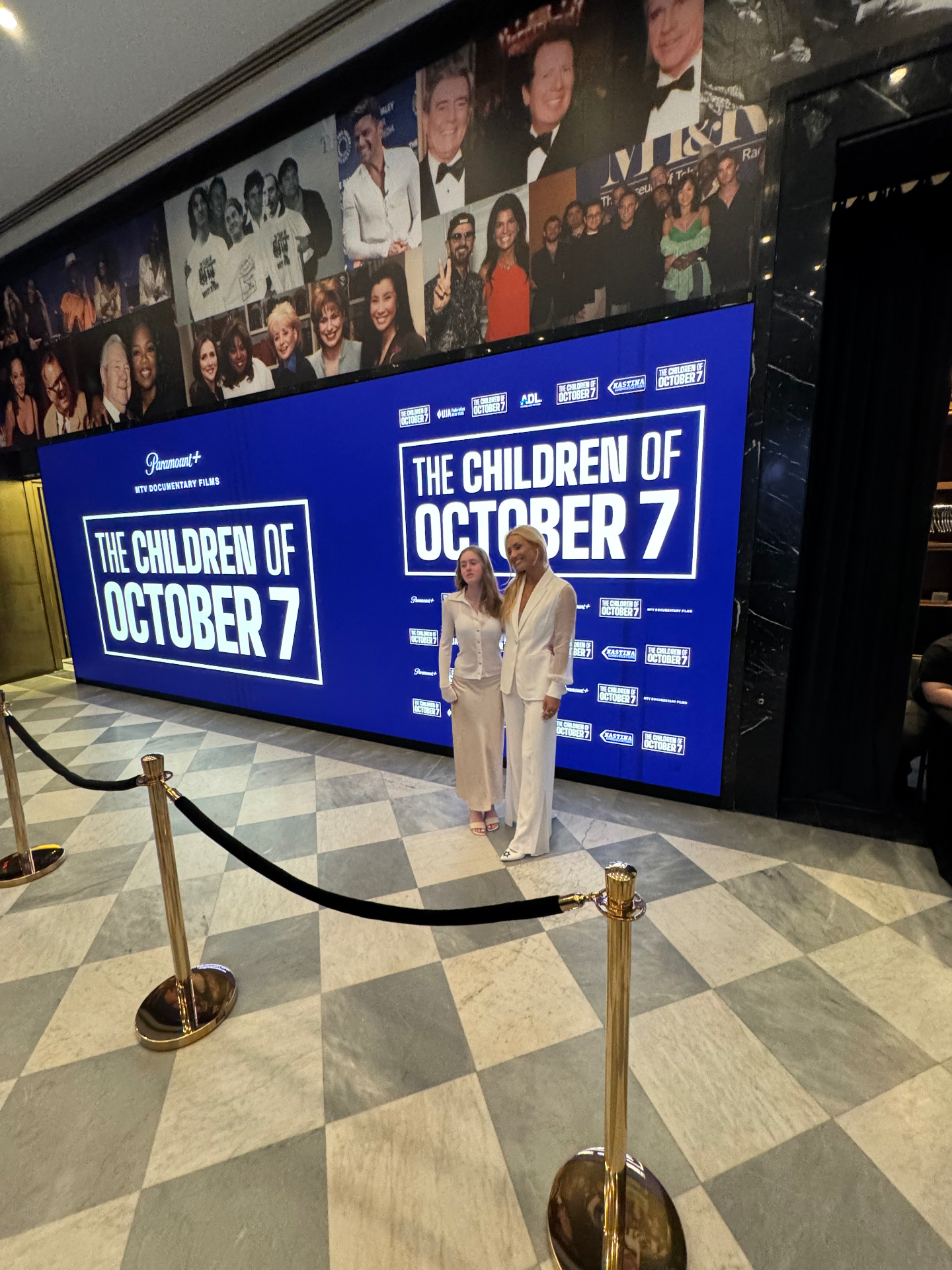 Talent pose in front of The Children of October 7 branded step-and-repeat at the New York premiere.