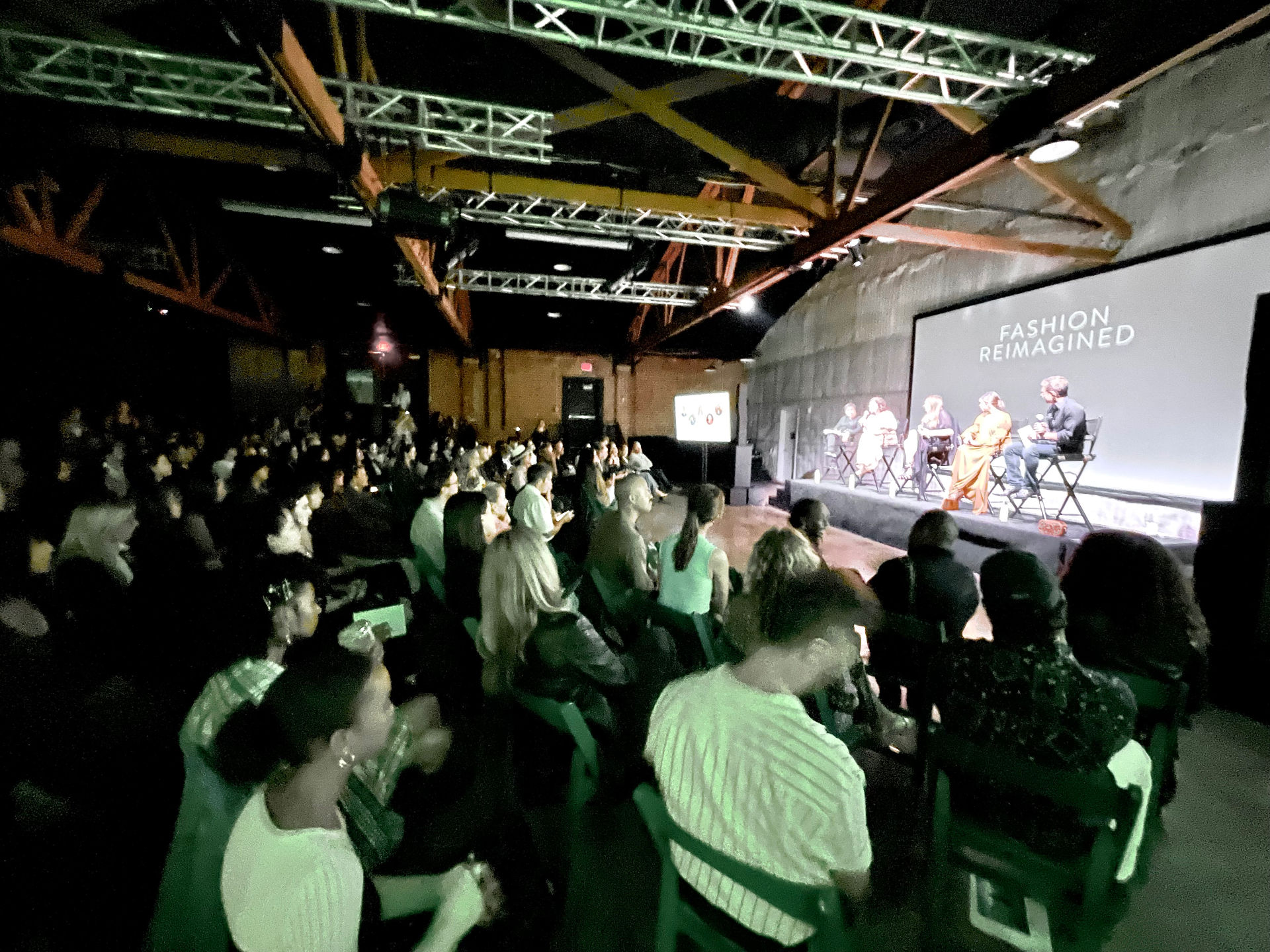 Capacity audience watches the Fashion Reimagined panel beneath stage trusses and a projected title card.